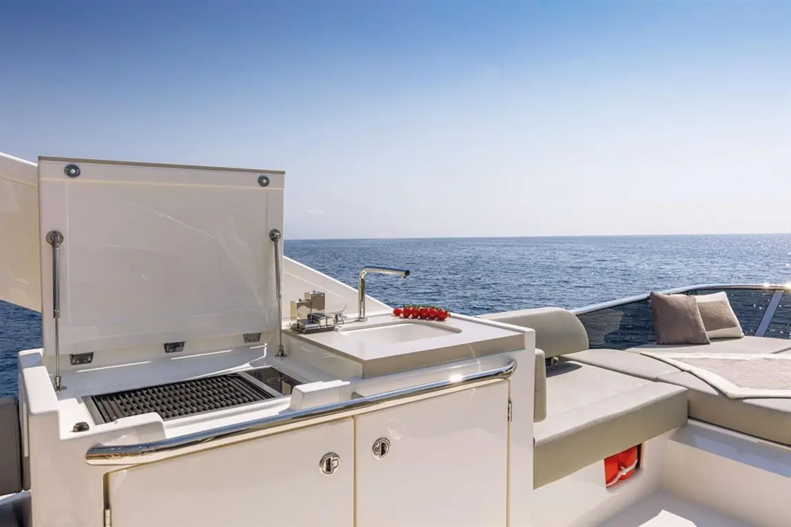 Outdoor yacht kitchen featuring a sink, barbecue grill, and a bowl of strawberries, overlooking the serene sea.